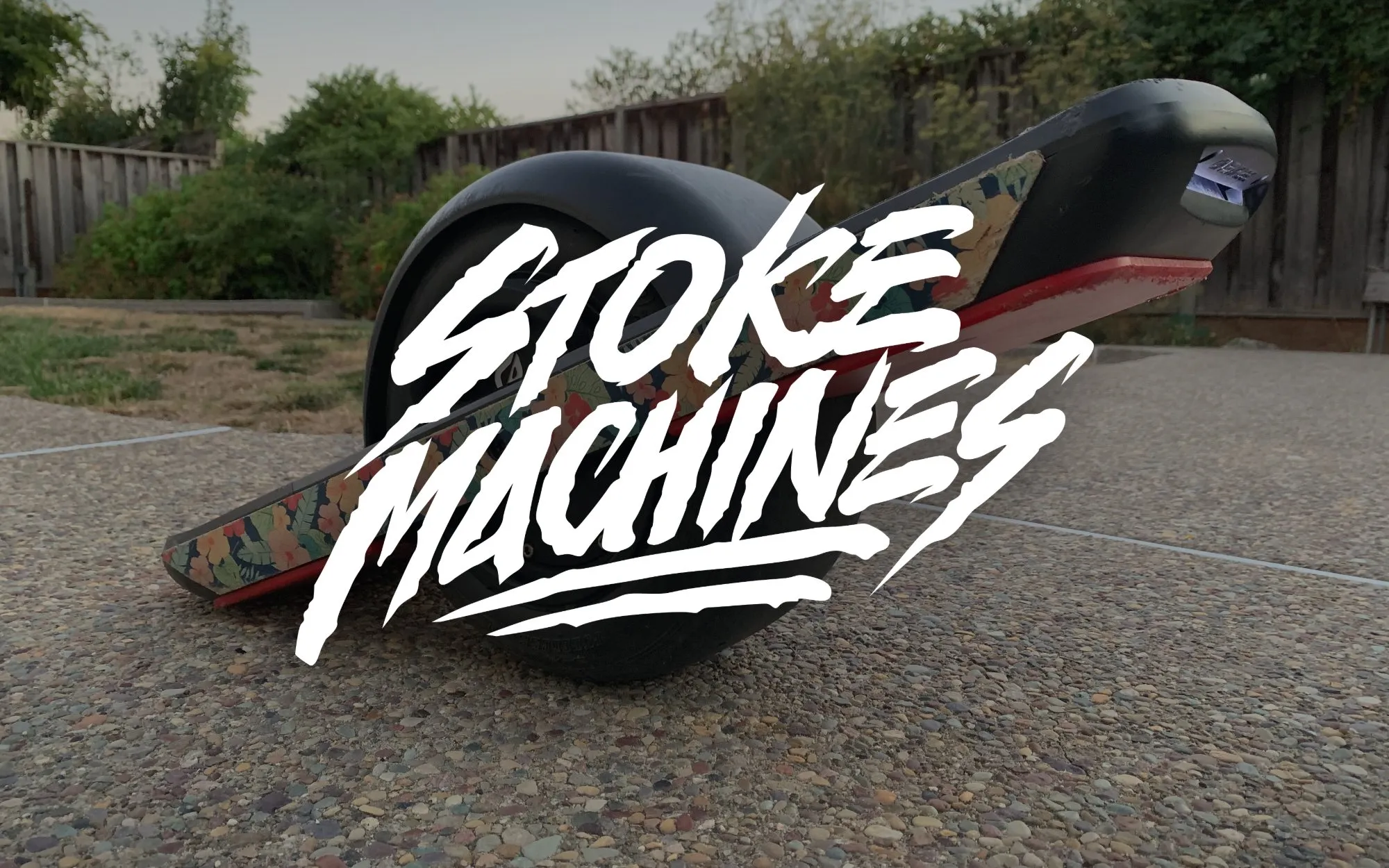 A Onewheel board with floral grip tape resting on sunlit concrete, with the Stoke Machines logo overlaid in white brush lettering.